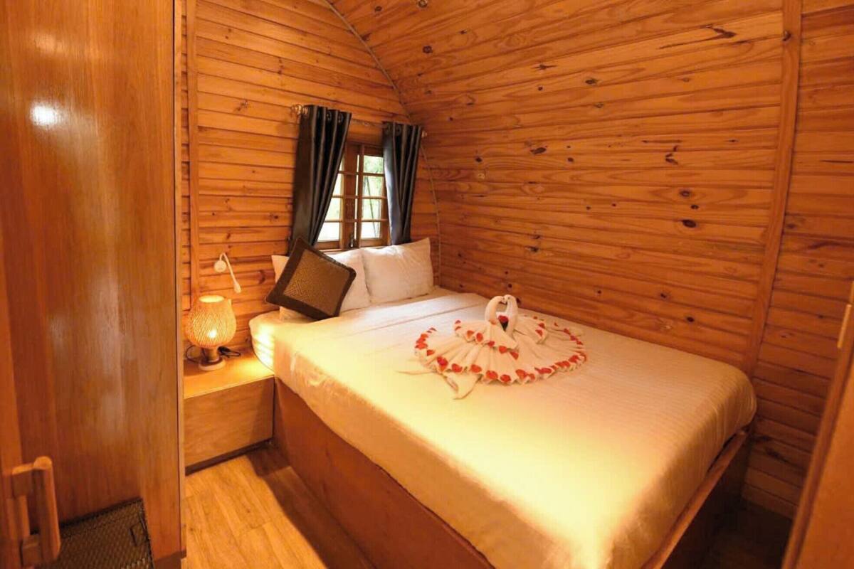 Une chambre dans un chalet en bois, avec un lit, une table de chevet, une lampe et une fenêtre avec des rideaux.