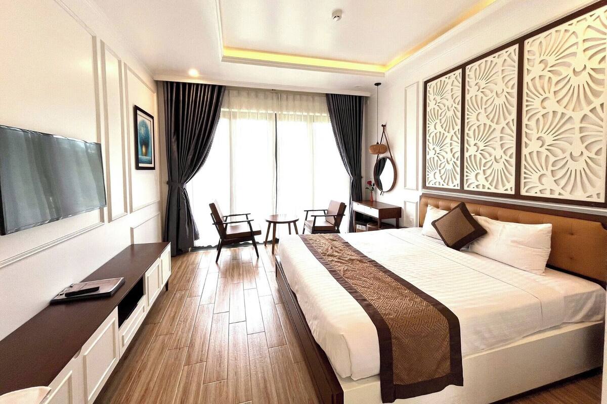 Une chambre d’hôtel comprenant un lit, une table de chevet, une chaise, un bureau, une télévision et un panneau décoratif mural.
