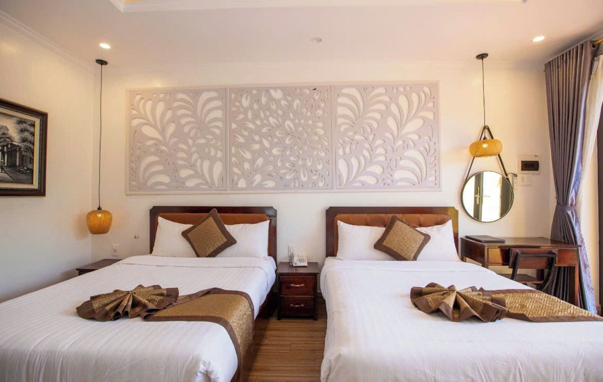 Habitación de hotel con dos camas, un panel decorativo en la pared, una mesita de noche con lámpara, un espejo y un cuadro enmarcado.