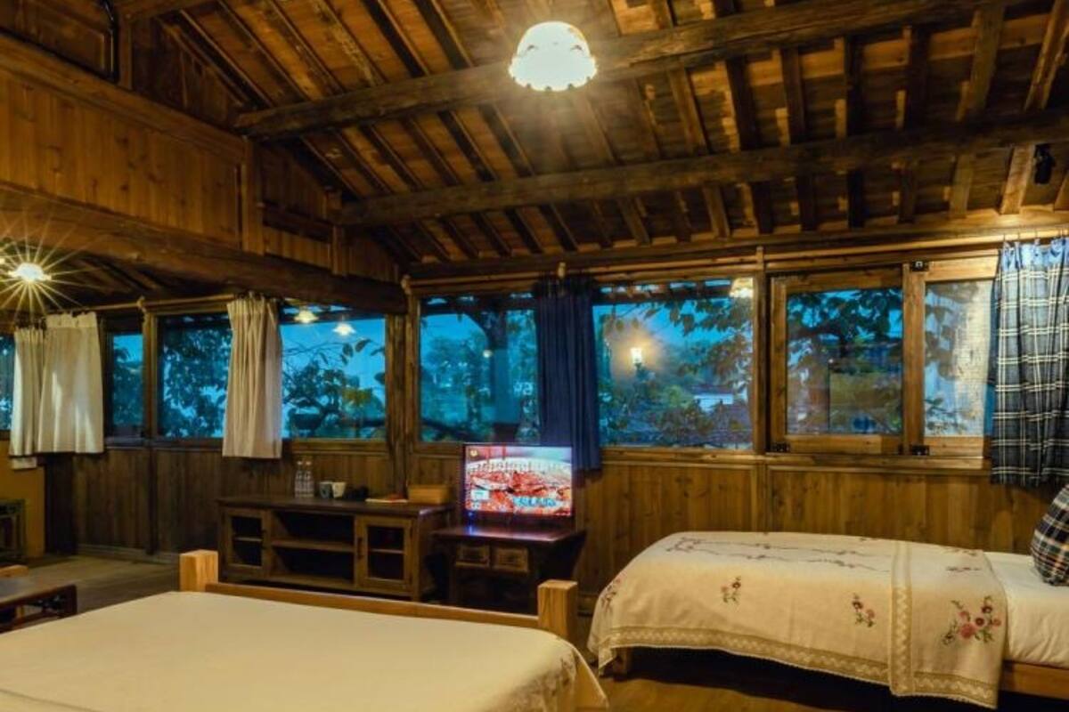 A rustic wooden room with a large bed, a smaller bed, a television, and a desk.