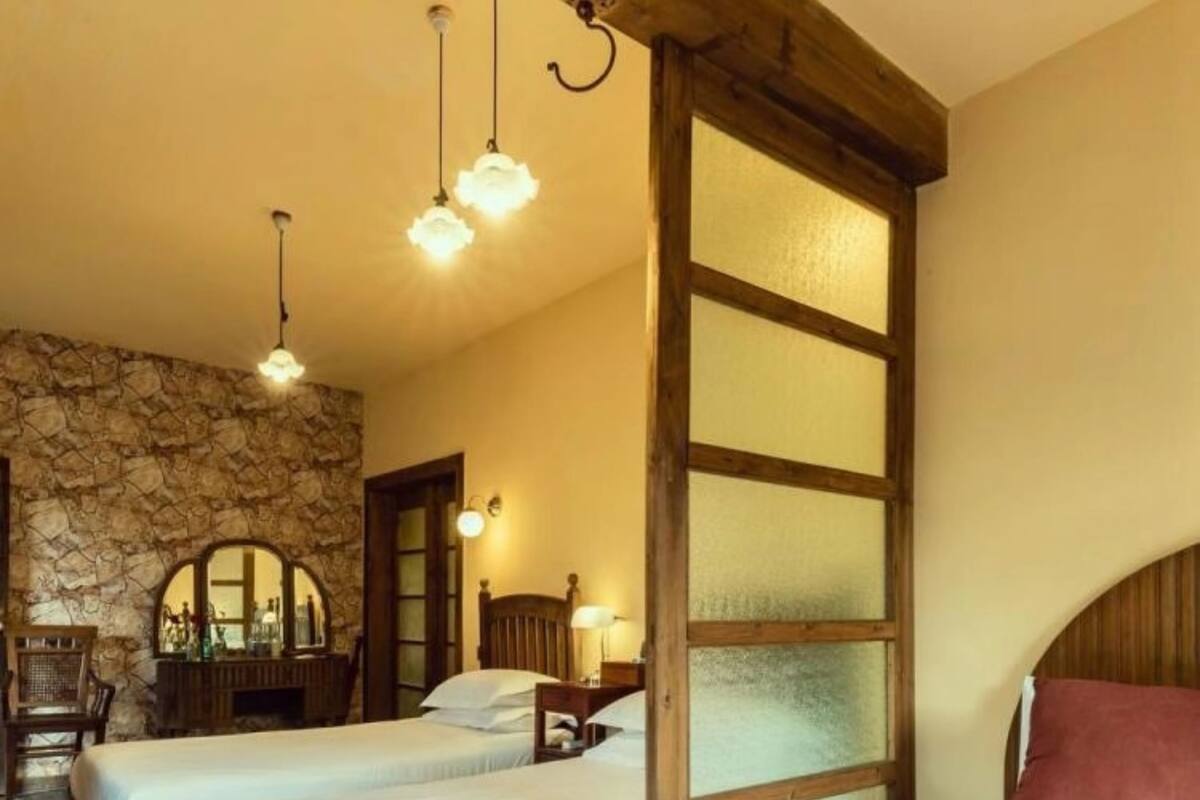 A room with two beds, a stone wall, wooden beams, and a mirror.