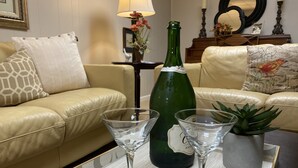 A living room with a beige sofa, two martini glasses, a green bottle, and a small potted plant on a tray.