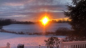 A snowy landscape with a sunset over a field, a lamp post, and a white fence.