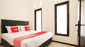 A neatly made bed with a red and white patterned blanket, two red pillows, and a dark headboard. - OYO Living 1743 Anie Residence (Surabaya)