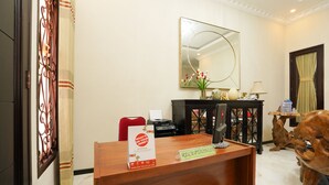 A reception desk with a sign, a mirror, a vase with flowers, and a wooden sculpture. - OYO Living 1743 Anie Residence (Surabaya)