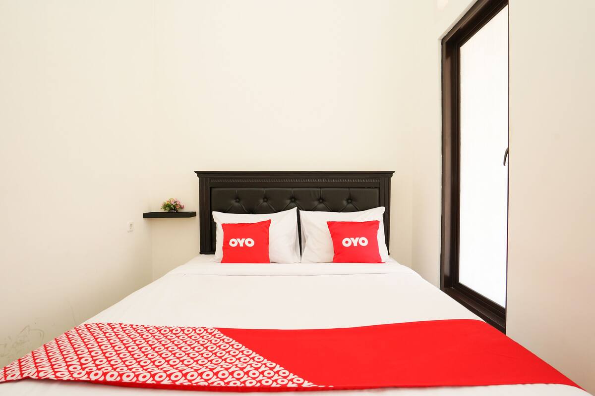 Una cama con una colcha blanca y roja estampada, dos almohadas rojas con la palabra "OYO" y un cabecero oscuro.