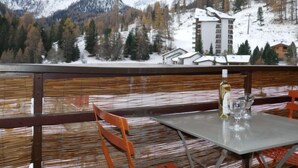 A table with a bottle and glasses, overlooking a snowy mountain landscape with buildings. - Rosablanche C32 by Interhome (Siviez-Nendaz)