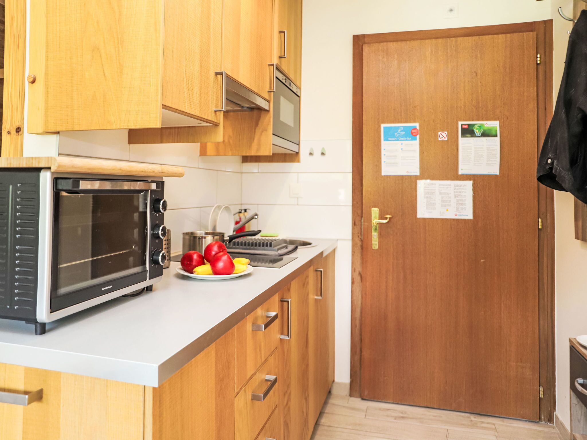 Una cocina con armarios de madera, un microondas, un fregadero y una puerta con avisos.