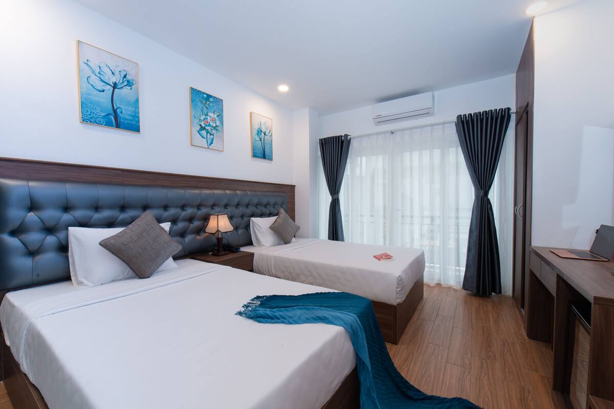 A hotel room with two beds, a wooden headboard, a desk, and a window with curtains.