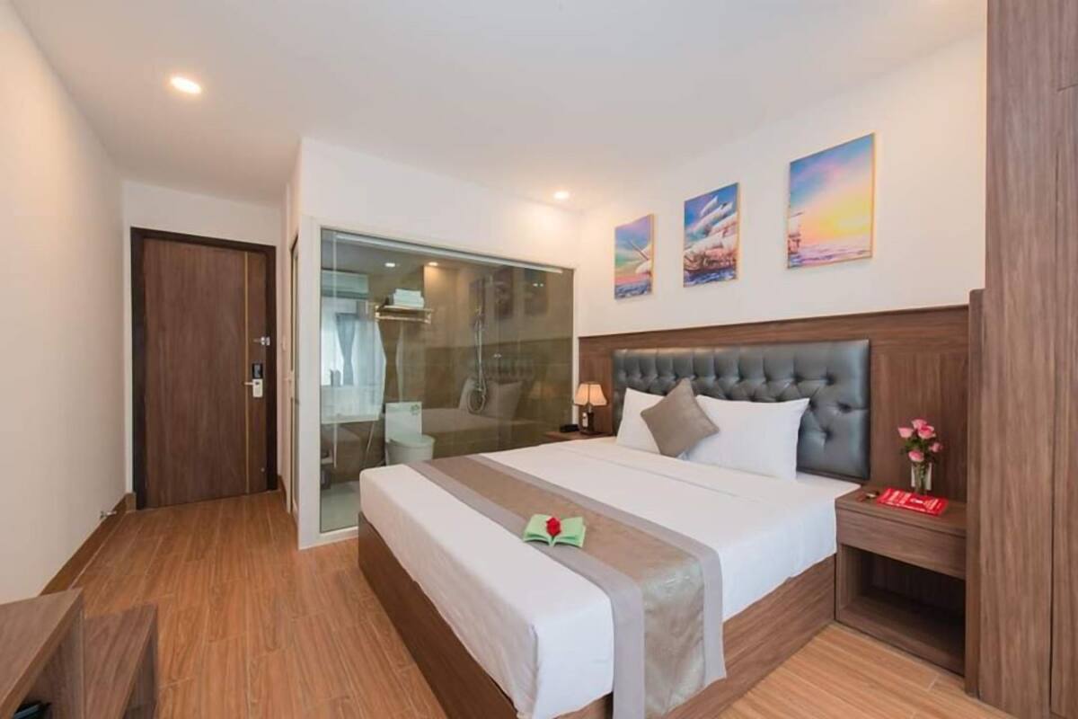 A hotel room with a large bed, a glass shower enclosure, wooden flooring, and a wooden headboard.