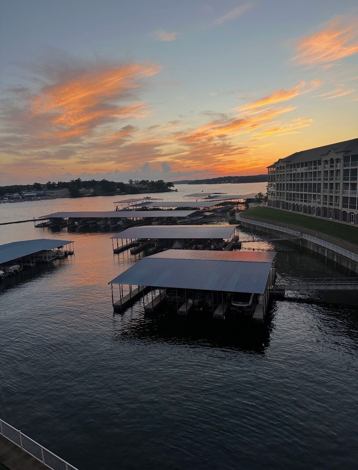 A waterfront property with multiple docked boats, a large building with a balcony, and a sunset view.