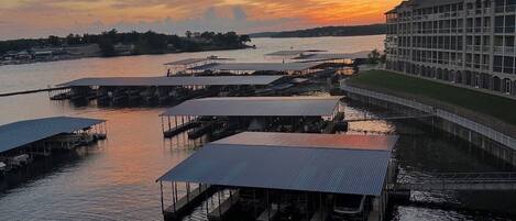 A waterfront property with multiple docked boats, a large building with a balcony, and a sunset view.
