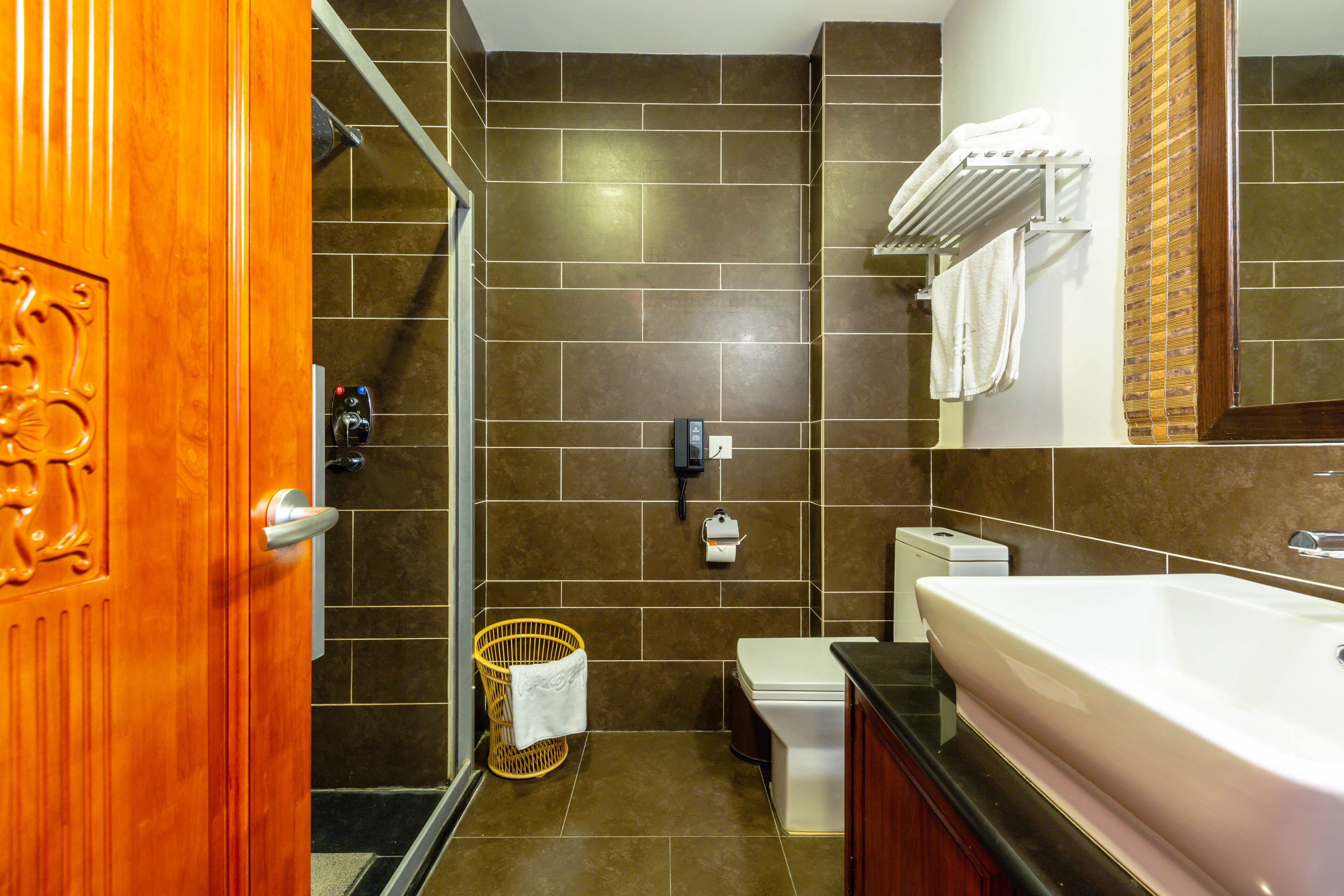 A bathroom with a wooden door, a shower, a toilet, a sink, and a towel rack.