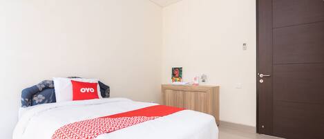 Habitación de hotel con cama, mesita de noche de madera, puerta y aire acondicionado de pared.