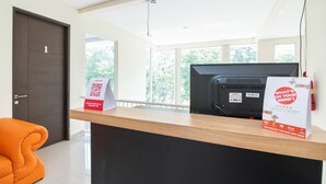 A reception desk with a computer monitor, a sign promoting a mobile app, and a view of the outdoors through large windows. - Hotel O Taman Dayu Villa Golf View (Prigen)