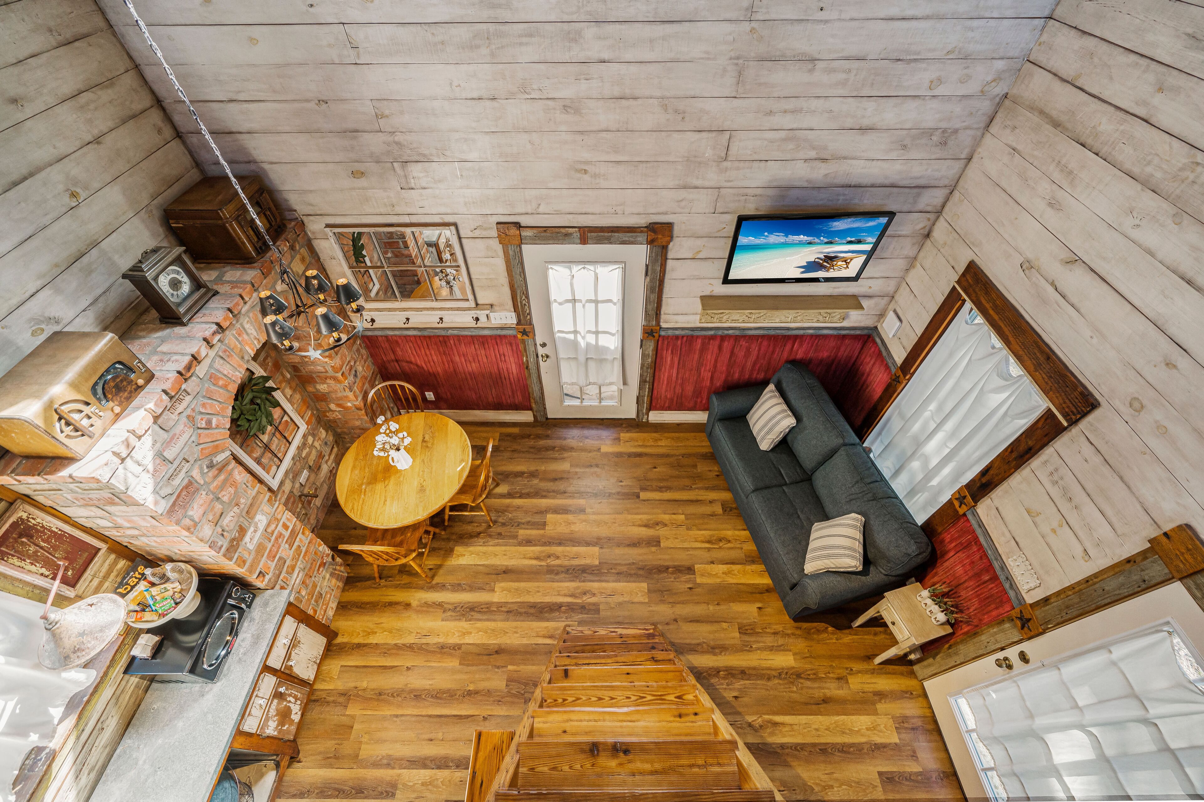 A cozy cabin interior with a wooden floor, a dining table, a sofa, and a television mounted on the wall.