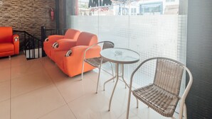 A modern lounge area with orange seating, a glass table, and a view of a tiled wall. - OYO 2010 Satria Guest House (Ambon)