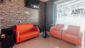 A hotel lobby with a modern design, featuring a large window, a flat-screen TV mounted on the wall, and two orange sofas. - OYO 2010 Satria Guest House (Ambon)