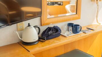 A hotel reception desk with a kettle, a black bag, two blue mugs, and a glass on a tray.