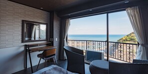 Une chambre d’hôtel avec une grande fenêtre donnant sur une plage, un bureau avec une chaise et un lit.