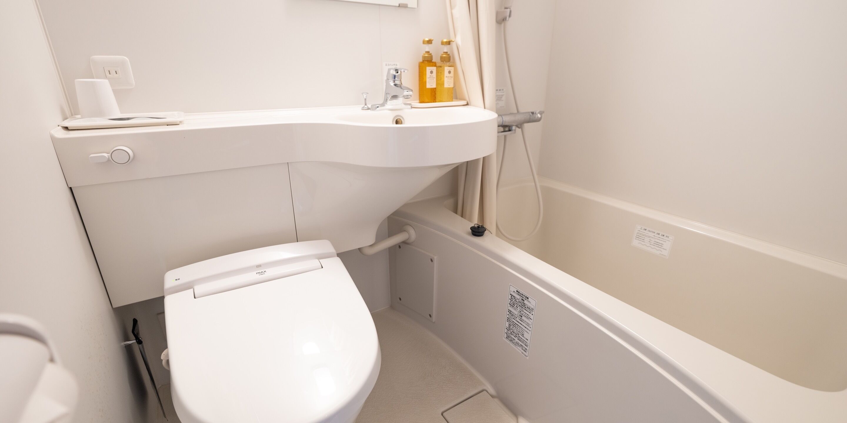 A bathroom with a white sink, toilet, and shower. There are toiletries on the sink and a shower curtain rod visible.