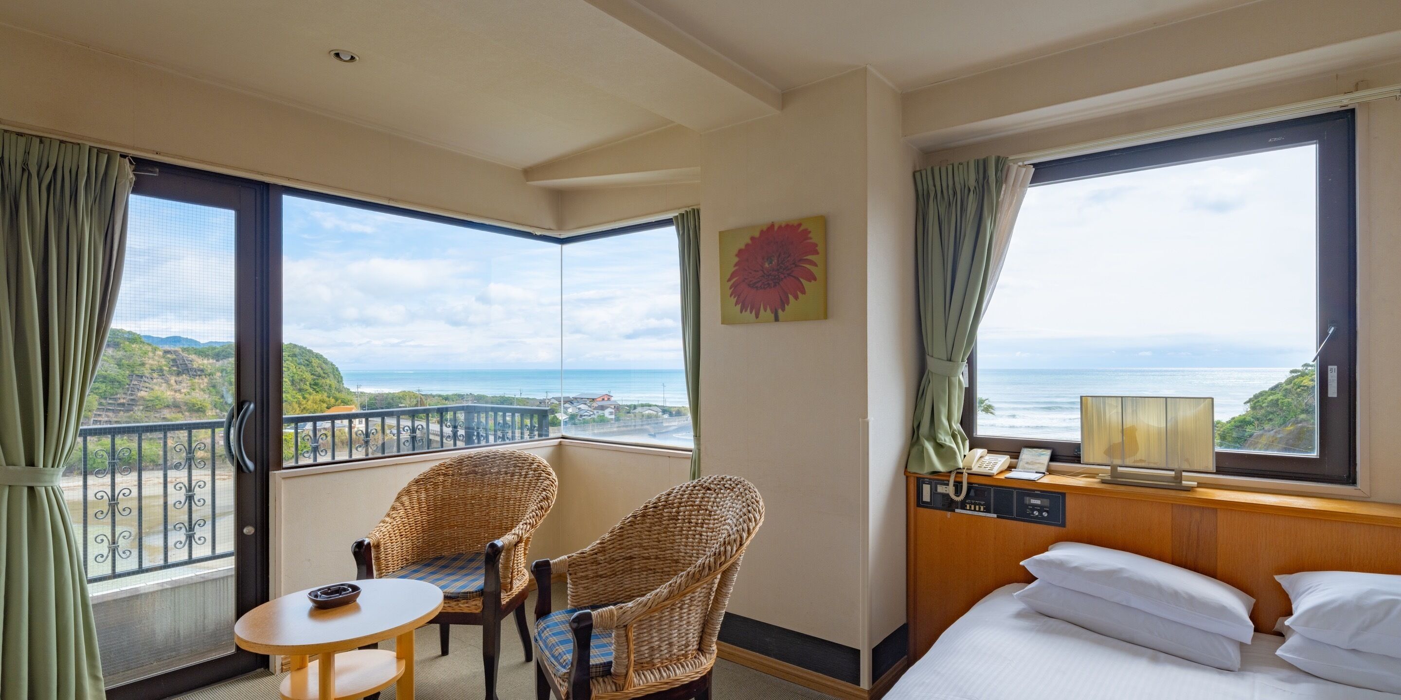 Une chambre d’hôtel avec un balcon, des fauteuils en osier, une petite table, un lit et une vue sur la mer.