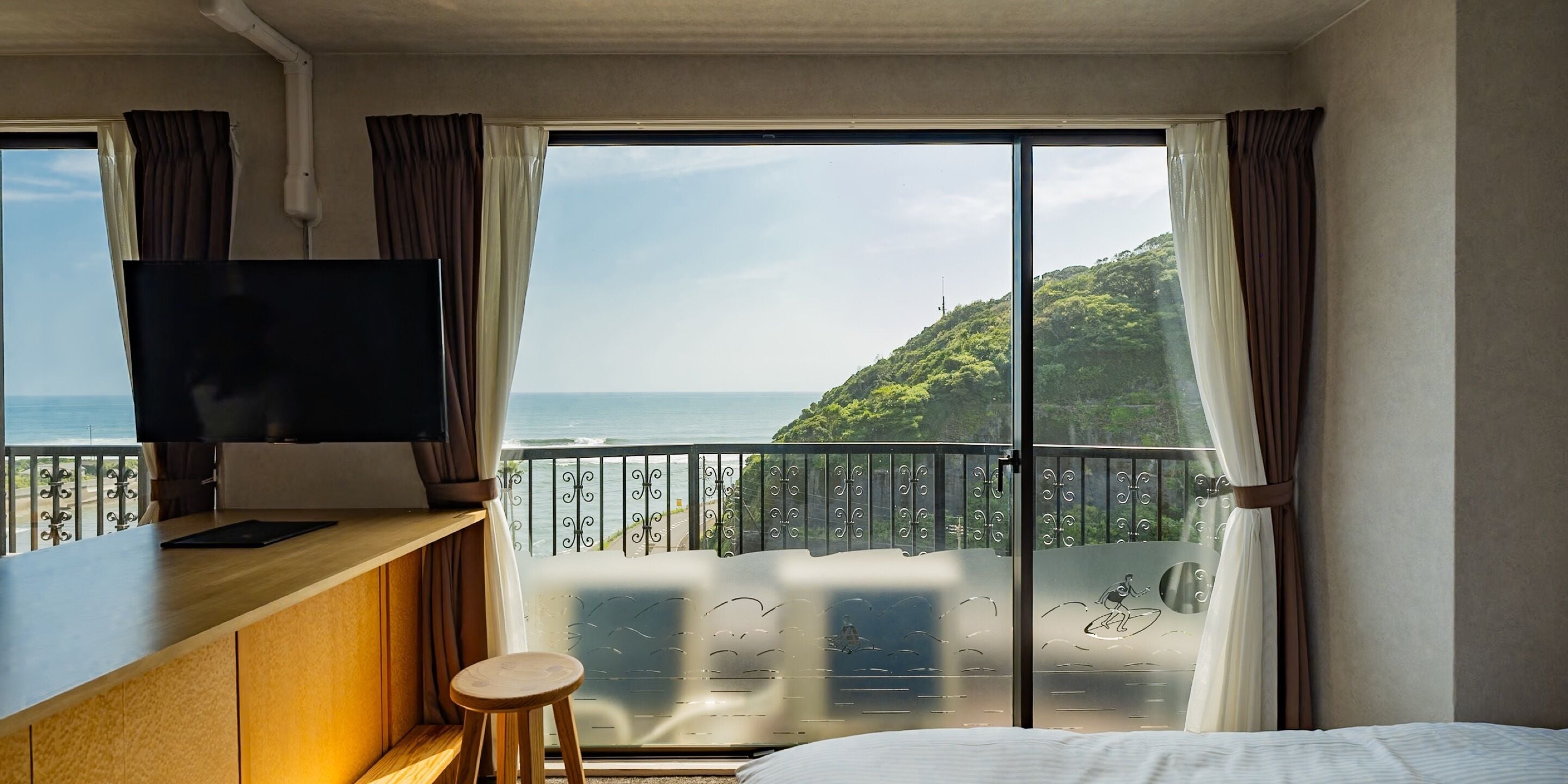 A hotel room with a balcony, a TV on a wooden desk, and a bed.