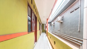 A narrow hallway with yellow and red walls, tiled floor, and a grey wall with air conditioning units. - OYO Living 1756 Amira Guest House (Bekasi)