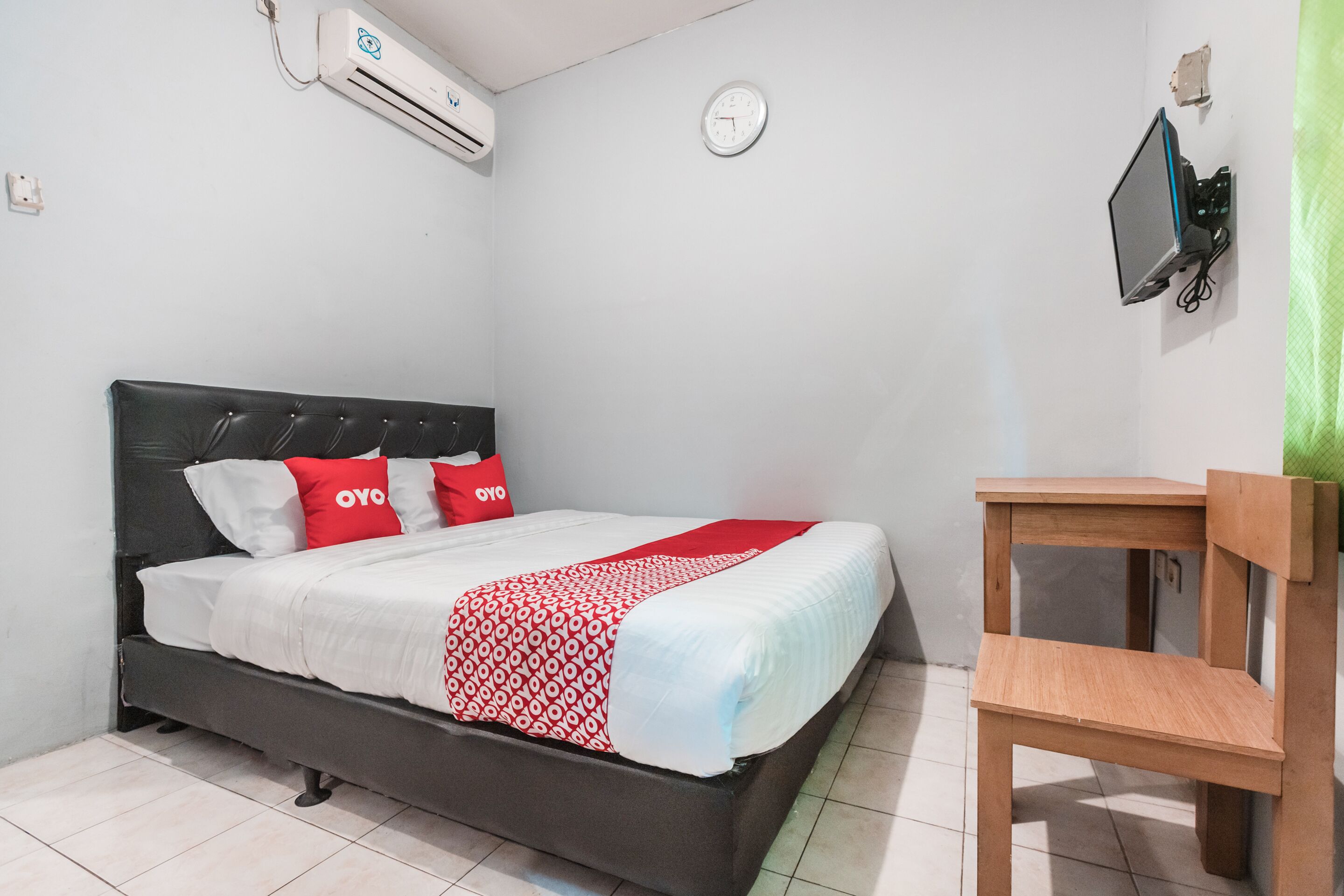 A bedroom with a bed, a wooden chair, a wall-mounted TV, and an air conditioner.