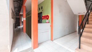 A hallway with a reception desk, a staircase, and a green wall with a sign. - OYO Living 1756 Amira Guest House (Bekasi)