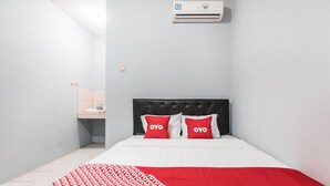 A hotel room with a bed, a red and white patterned blanket, a black headboard, and two red pillows with the word "OYO" on them. - OYO Living 1756 Amira Guest House (Bekasi)