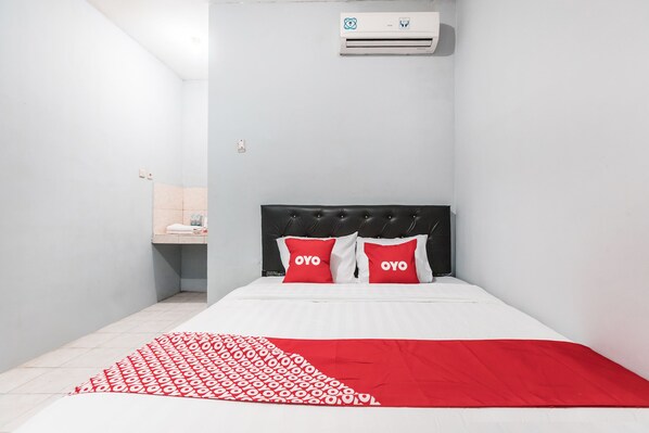 A hotel room with a bed, a red and white patterned blanket, a black headboard, and two red pillows with the word "OYO" on them.