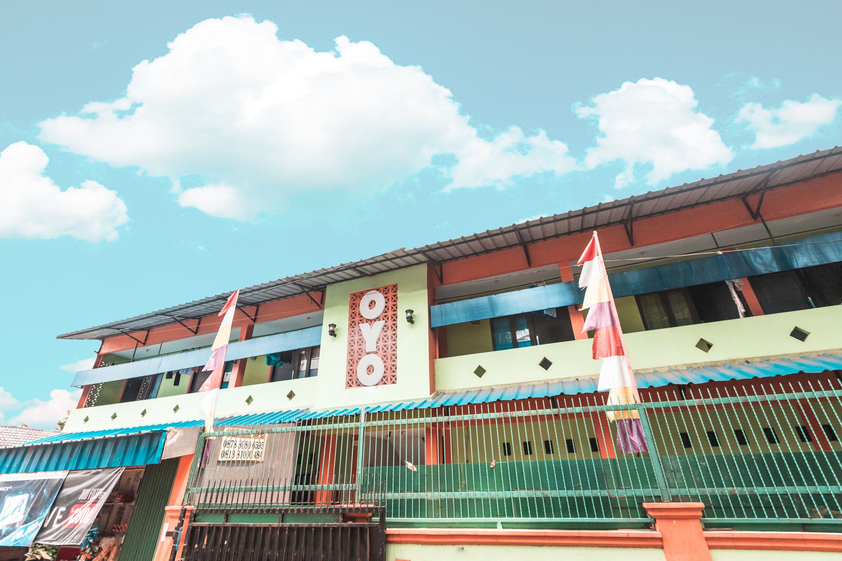 A multi-story building with a green and red facade, a prominent clock, and a flag on the roof.