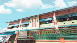 A multi-story building with a green and red facade, a prominent clock, and a flag on the roof. - OYO Living 1756 Amira Guest House (Bekasi)
