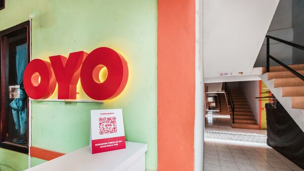 A reception area with a large 'OYO' sign, a white reception desk, and a staircase in the background. - OYO Living 1756 Amira Guest House (Bekasi)