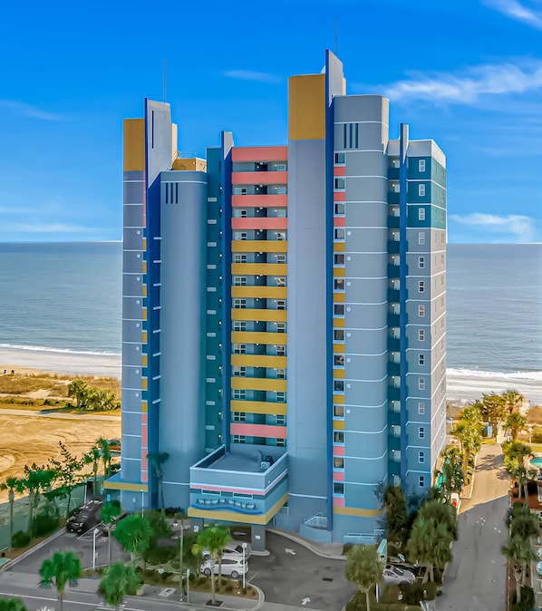 A multi-story hotel with balconies, a parking area, and a view of the ocean.