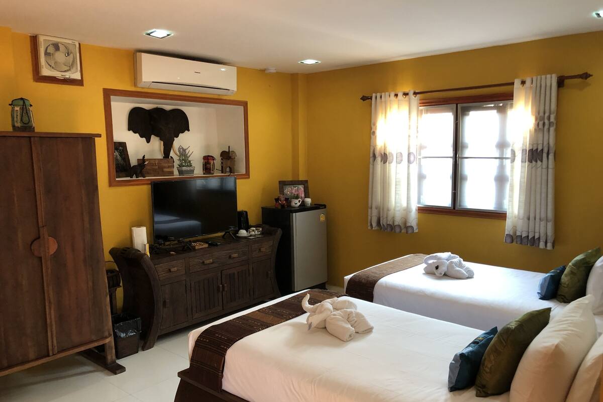 A hotel room with two beds, a wooden cabinet, a television, and an air conditioning unit.