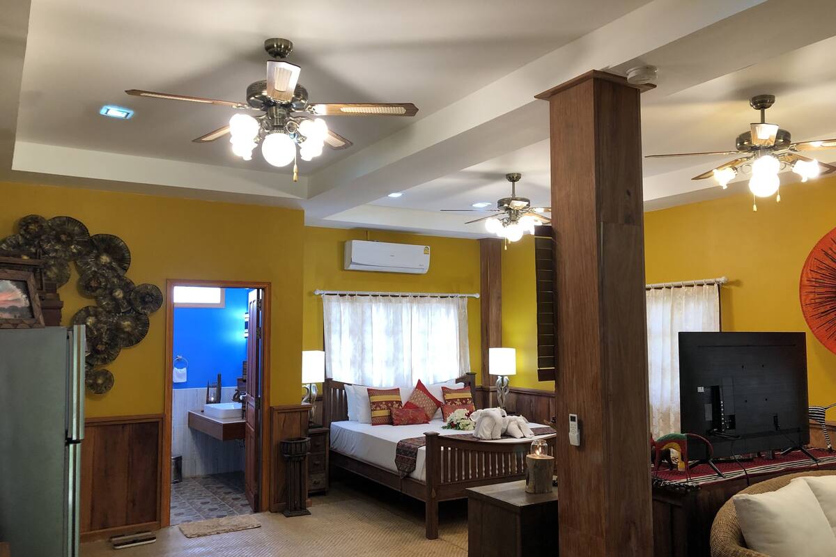A hotel room with a bed, bedside tables, a TV, a wooden pillar, and a ceiling fan.