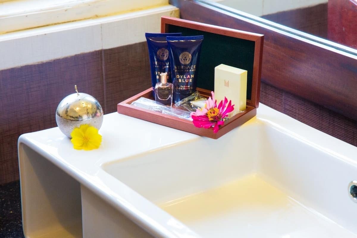 A bathroom with a white sink, a decorative mirror, and toiletries in a wooden tray.