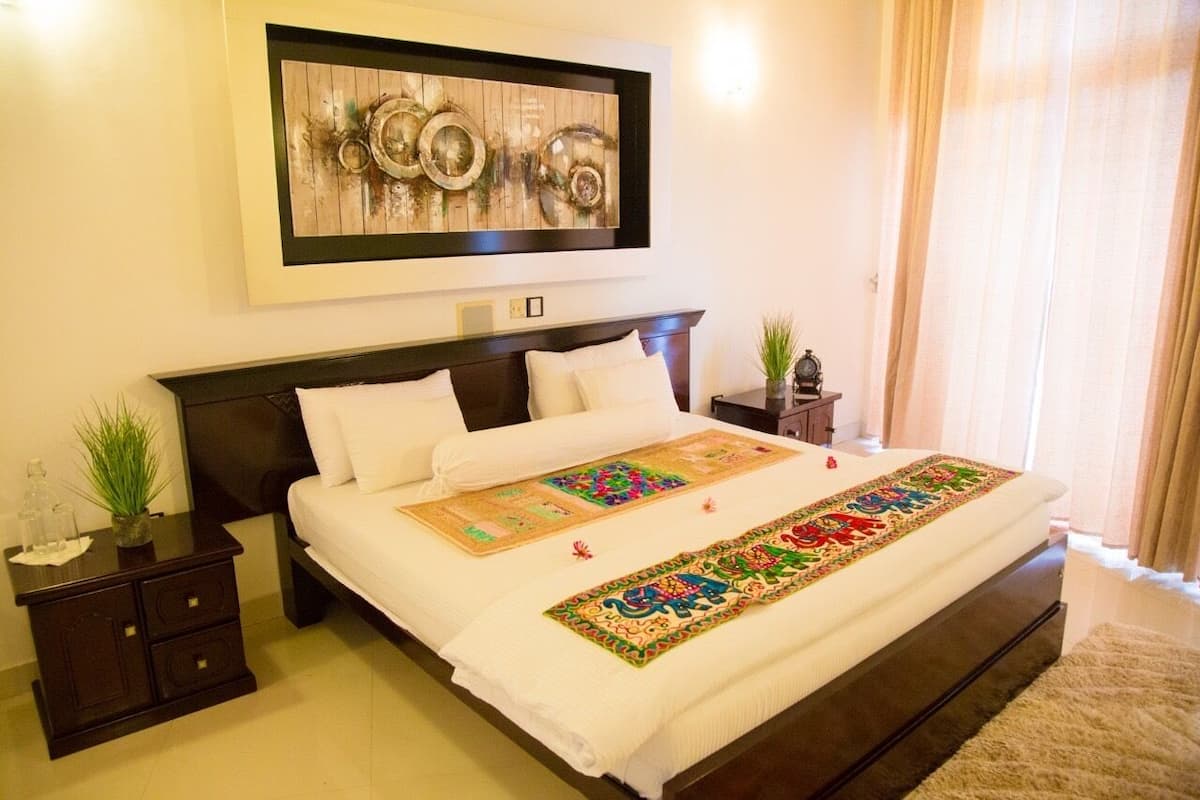 A neatly made bed with a decorative runner, a dark wooden headboard, and a small bedside table with a plant.