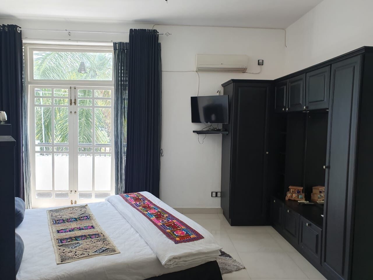 Un dormitorio con cama, televisión, armario y ventana con cortinas.