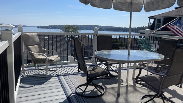 A deck with a round table and chairs, a large umbrella, and a view of a body of water. - Weirs Beach - PRIME LOCATION!!!  (Weirs Beach)