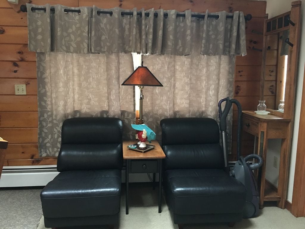 A room with two black leather chairs, a small wooden table with a lamp, and a vacuum cleaner.