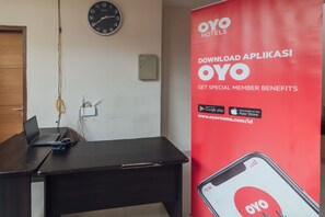 Un comptoir d’accueil d’hôtel avec un ordinateur portable, une horloge et une bannière publicitaire rouge pour la chaîne OYO Hotels.