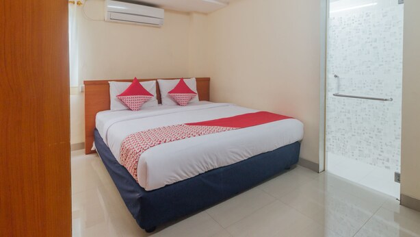 Habitación de hotel con cama, cabecera de madera, colcha estampada en rojo y blanco, y suelo de baldosas.