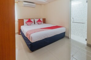 Une chambre d’hôtel avec un lit, une tête de lit en bois, une couvre-lit à motifs rouges et blancs, et un sol carrelé.