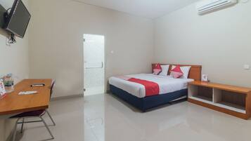 A hotel room with a bed, a desk, a chair, a TV, and an air conditioning unit.