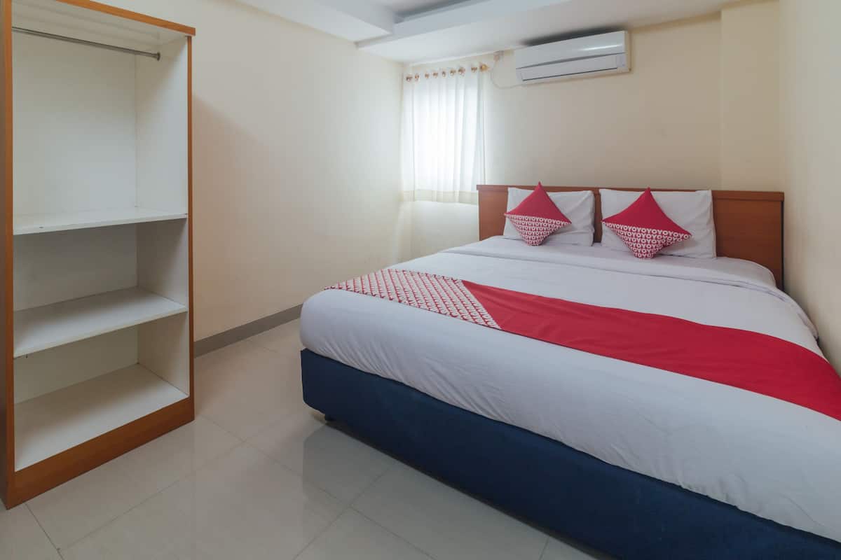 A hotel room with a bed, a wardrobe, and an air conditioning unit.