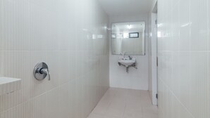 Un baño moderno con paredes de azulejos blancos, un lavabo y un espejo.