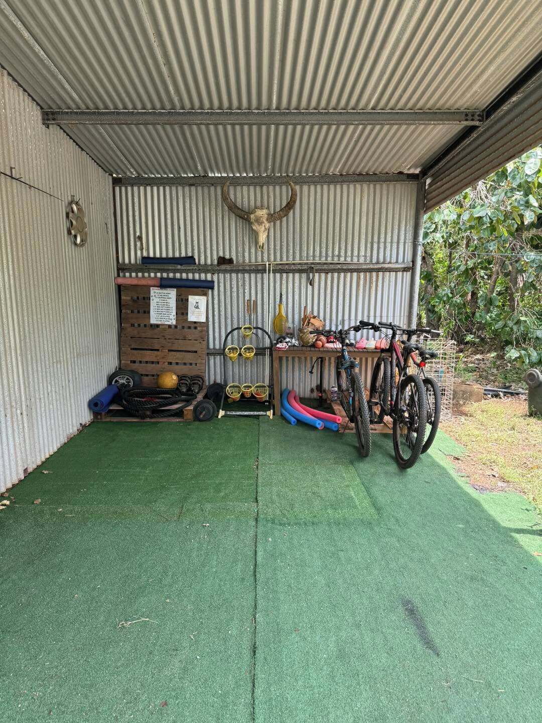 Eine Garage mit Vordach, ausgestattet mit grünem Kunstrasen, einem Motorrad, einem Fahrrad und diversen Werkzeugen und Geräten.